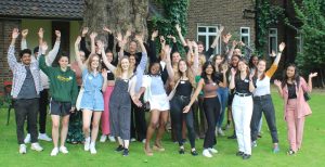 A group of 30 young people cheering together outside in a garden area at a training day during their internship.