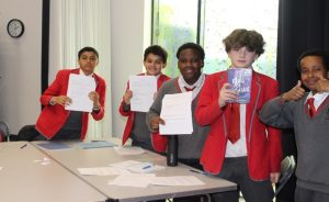 Four City London Academy- Highgate Hill students posing for a photograph. Three are holding up their writing and one is posing with one of Nathanel Lessore's books, King of Nothing