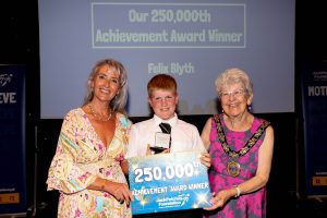 A young boy holding a certificate with the words '250,000th Achievement Award winner' standing with two women, Councillor Jannetta Sosin, Mayor of Chelmsford and Grants Manager Jane