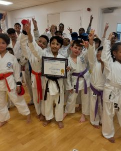 Group of young people dressed in karate uniform. In the middle is a boy holding a certificate.