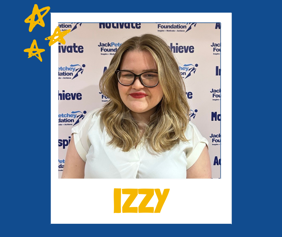 A portrait-style image of a person with shoulder-length curled blonde hair, wearing a short-sleeved white top. The background features a step‑and‑repeat banner with the Jack Petchey Foundation logo and words like “Achieve,” “Motivate,” and “Inspire.” The photo is framed like a polaroid with a blue border, yellow star doodles in the top left corner, and the name “IZZY” written in bold yellow letters at the bottom.