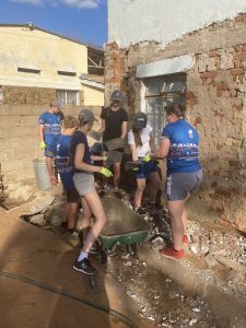 Volunteers mixing cement and clearing rubble beside a damaged building during a community repair project.
