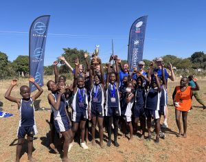 Children celebrating with a trophy alongside volunteers, surrounded by event banners on a grassy field.