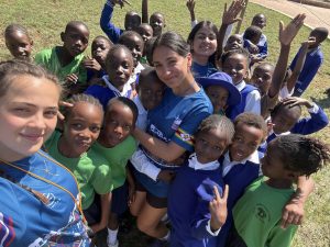 A volunteer surrounded by schoolchildren in green and blue uniforms, all gathered closely together.